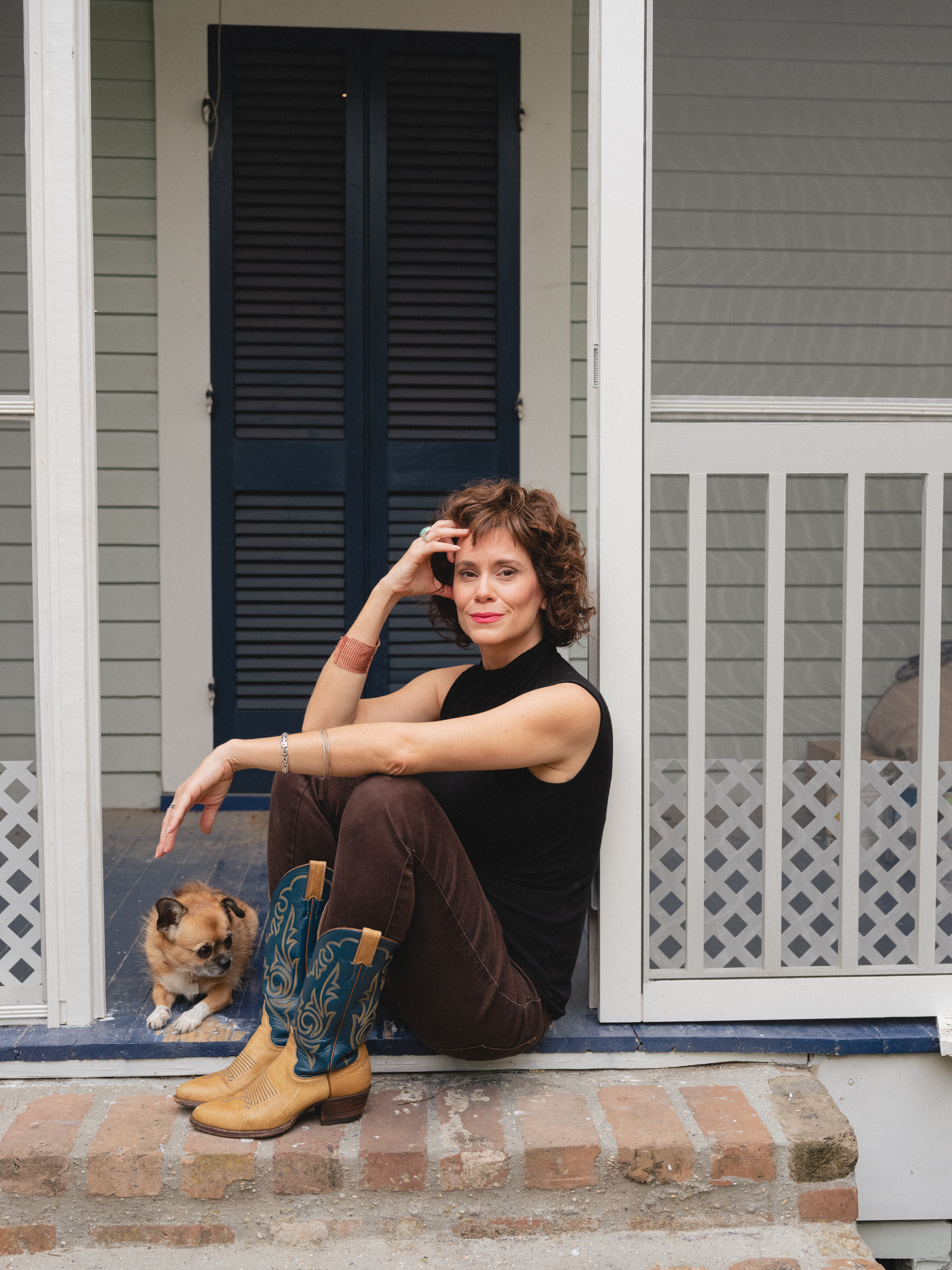Fair-skinned woman with dark blond hair sits on a porch beside a small dog..